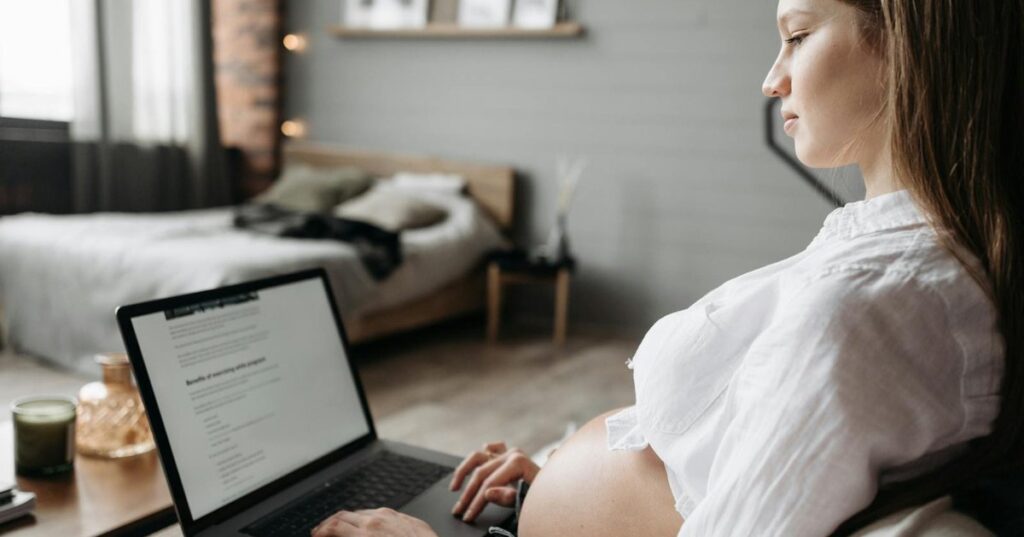 Mulher grávida trabalhando com notebook em casa representando o salário-maternidade