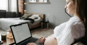 Mulher grávida trabalhando com notebook em casa representando o salário-maternidade