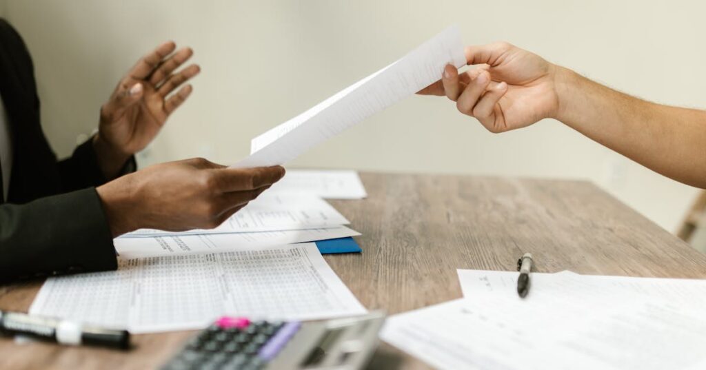 Pessoas trocando documentos sobre uma mesa com calculadora durante uma audiência de conciliação por superendividamento