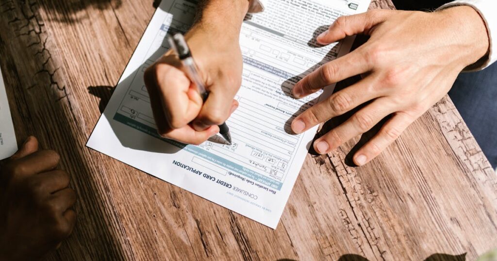 Mãos de adulto assinando contrato bancário sobre mesa de madeira