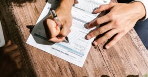 Mãos de adulto assinando contrato bancário sobre mesa de madeira