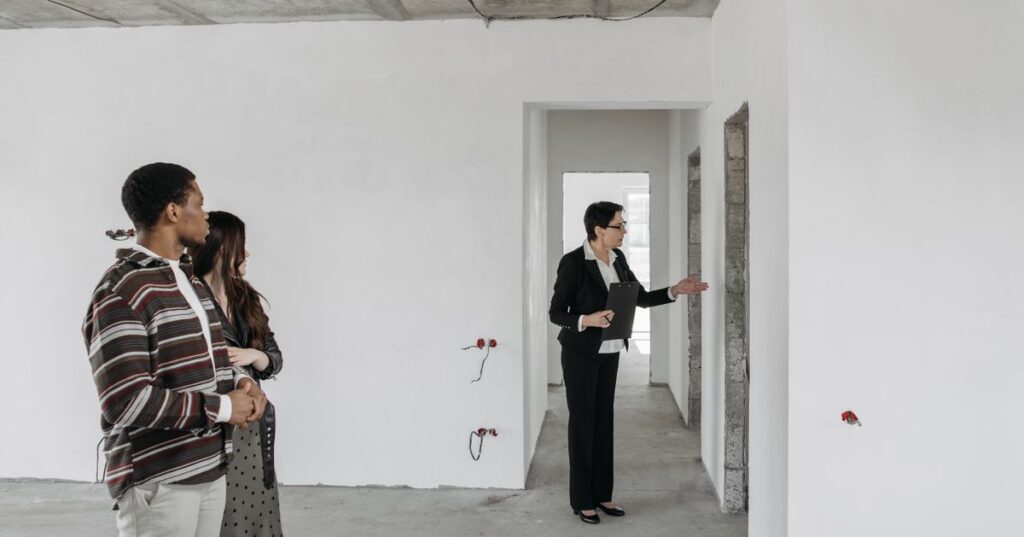 Casal adulto visitando apartamento em obra com corretor, representando compra de imóvel na planta