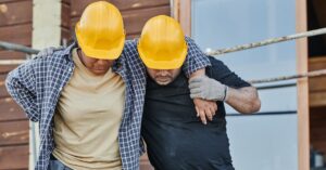 Trabalhadores com capacete auxiliam colega acidentado em obra, tema do auxílio-acidente do INSS