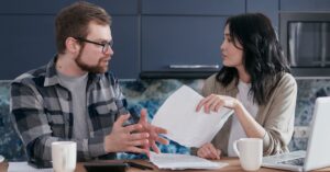 Casal adulto conversando a mesa com documentos e contas sobre plano de pagamento de dividas