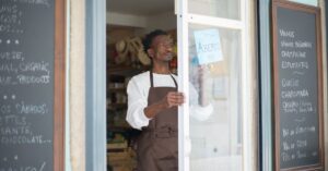 Comerciante adulto abrindo a loja com placa de aberto no ponto comercial